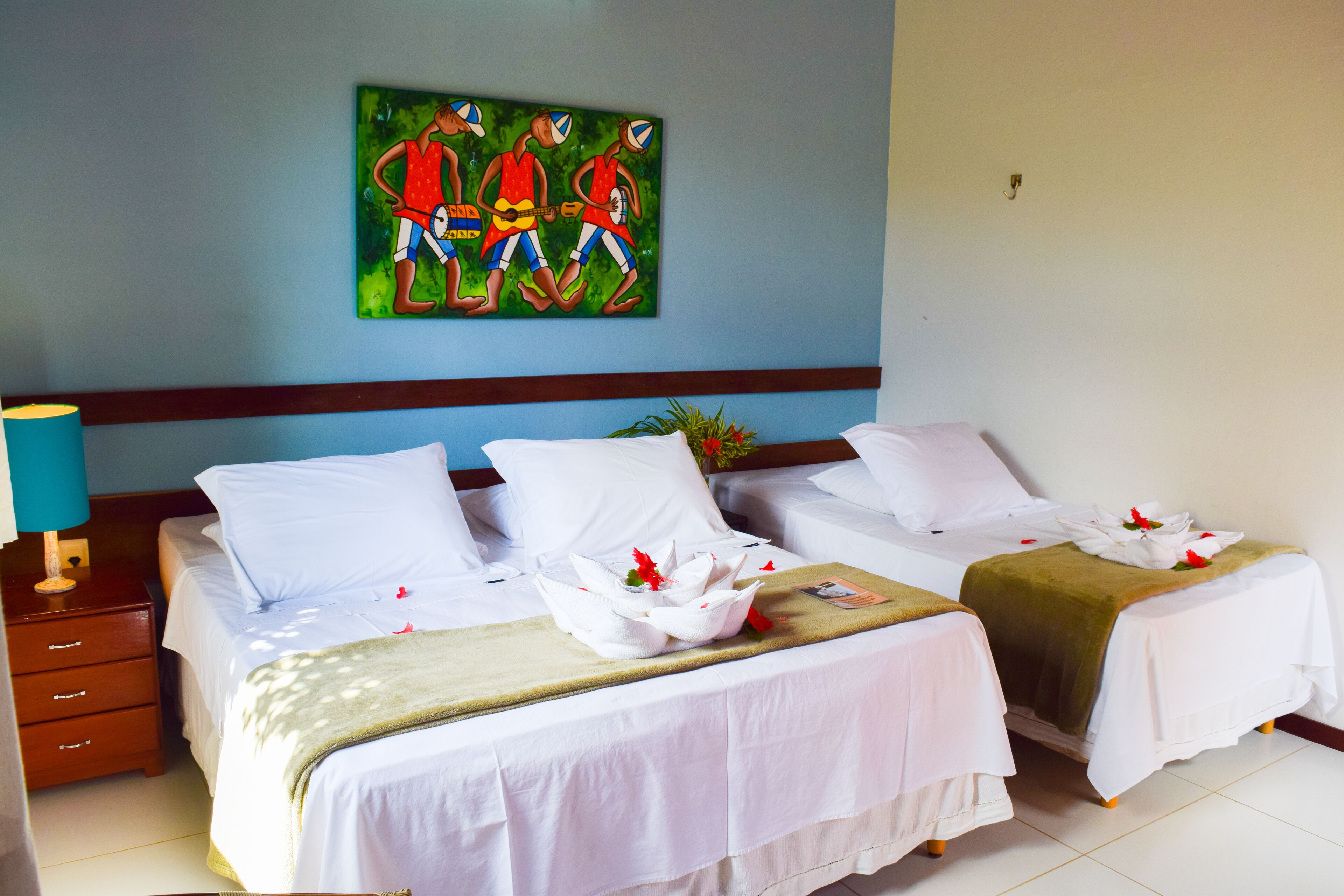 A hotel room with two beds, white linens, a painting on the wall, and a nightstand with a lamp.