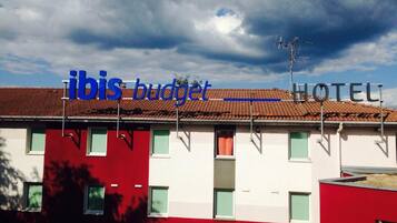 A two-story building with a red and white facade, a flat roof, and a sign that reads "ibis budget HOTEL".