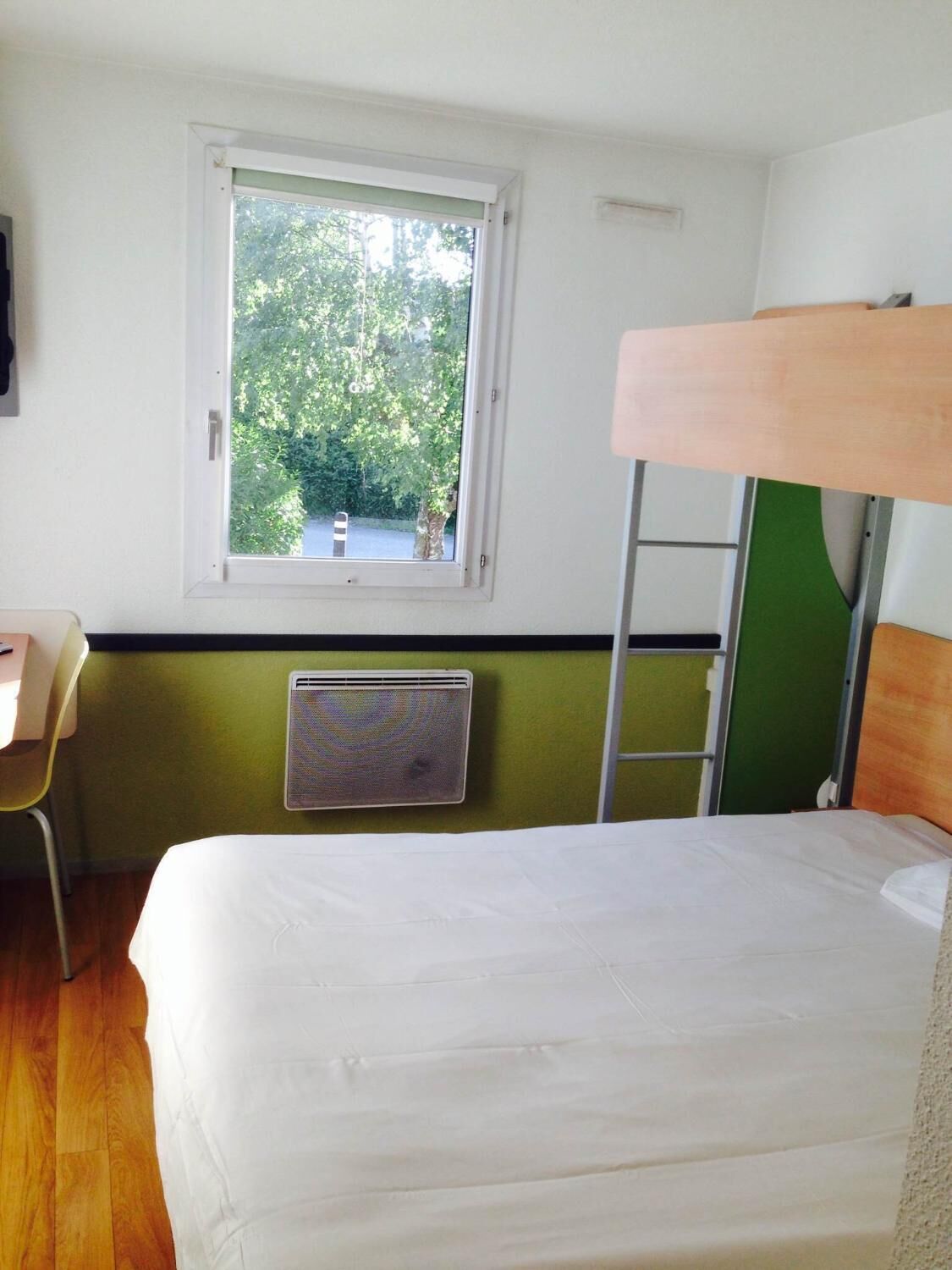 A room with a bunk bed, a desk, a chair, a radiator, and a window with a view of trees.