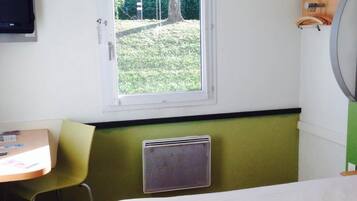 Ein Zimmer mit Bett, Schreibtisch, Stuhl, einem Fenster mit Blick auf Grünflächen und einem Wand-Fernseher.