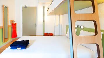 A hotel room with a bunk bed, a mirror with cut-out sections, a bed with a white sheet, a red dress hanging on the wall, and a red bag on the floor.