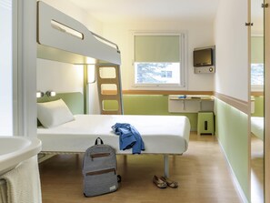 Een kleine kamer met stapelbedden, een bureau, een stoel, een tafeltje en een raam.