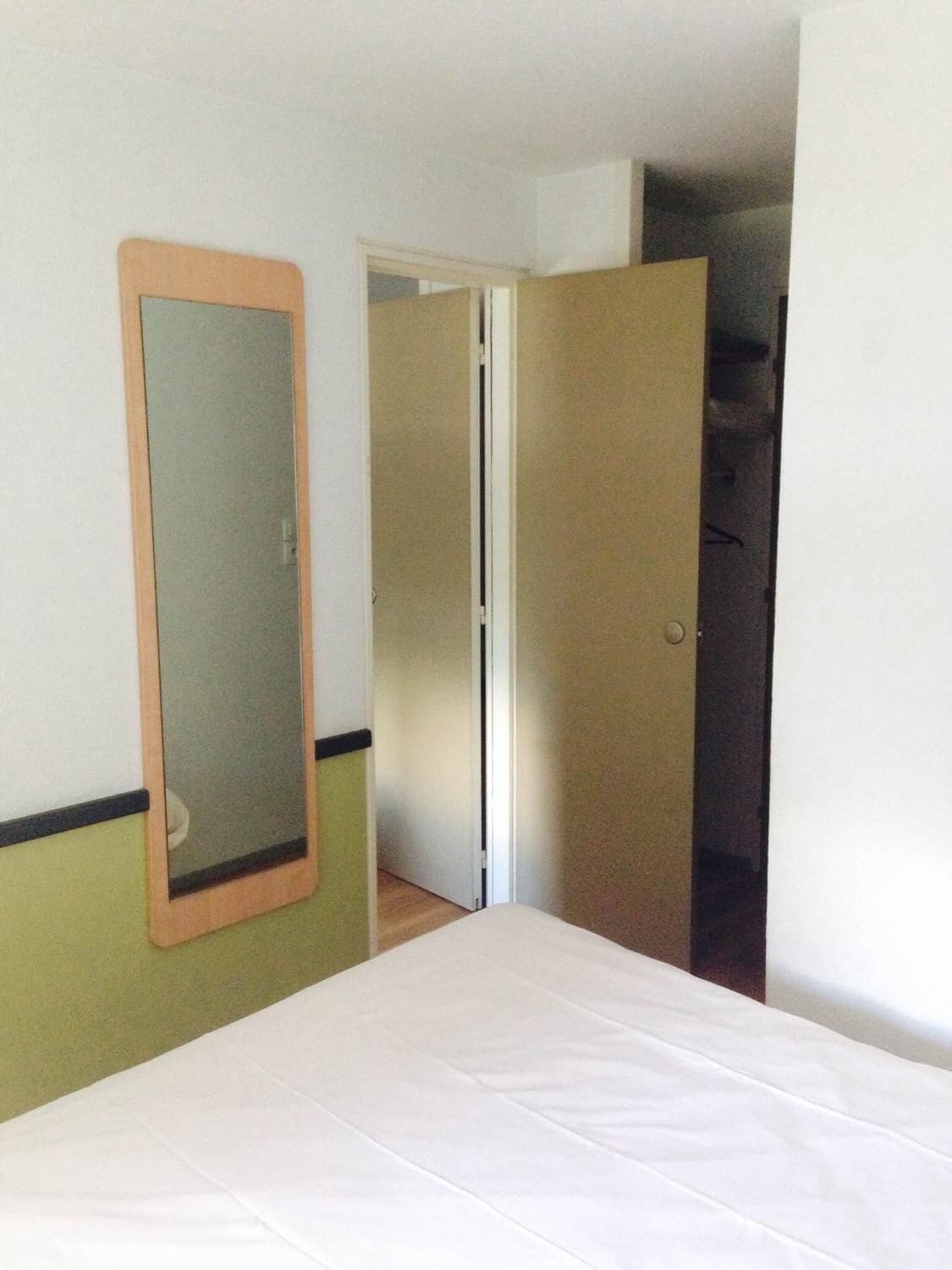 Una habitación de hotel con una cama, un espejo y una puerta que da a un armario.