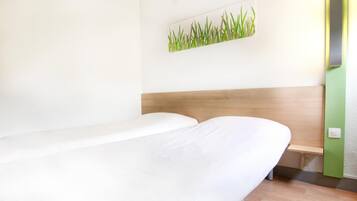 Habitación de hotel con cabecera de madera, una cama individual y un cuadro colgado en la pared con un diseño de hierba.