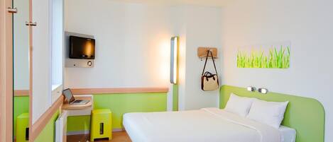 Una habitación de hotel moderna con una cama, un escritorio, una silla, un televisor y una lámpara fijada a la pared.