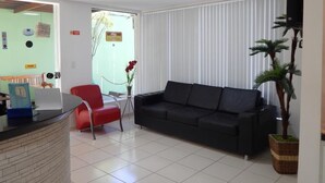 A modern living room with a black sofa, red chair, and a reception desk. - Perolas Do Mar Pousada (Maceio)