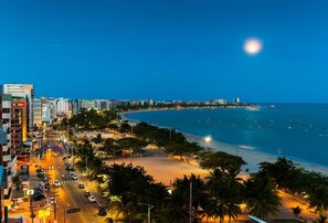 Un paisaje urbano costero nocturno con una playa, edificios y una luna creciente.