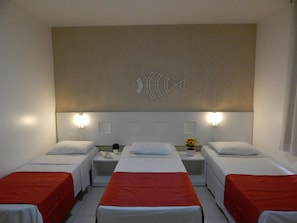 Een hotelkamer met drie eenpersoonsbedden, elk met een rode sprei, een witte hoofdbord en een visdecoratie aan de muur.