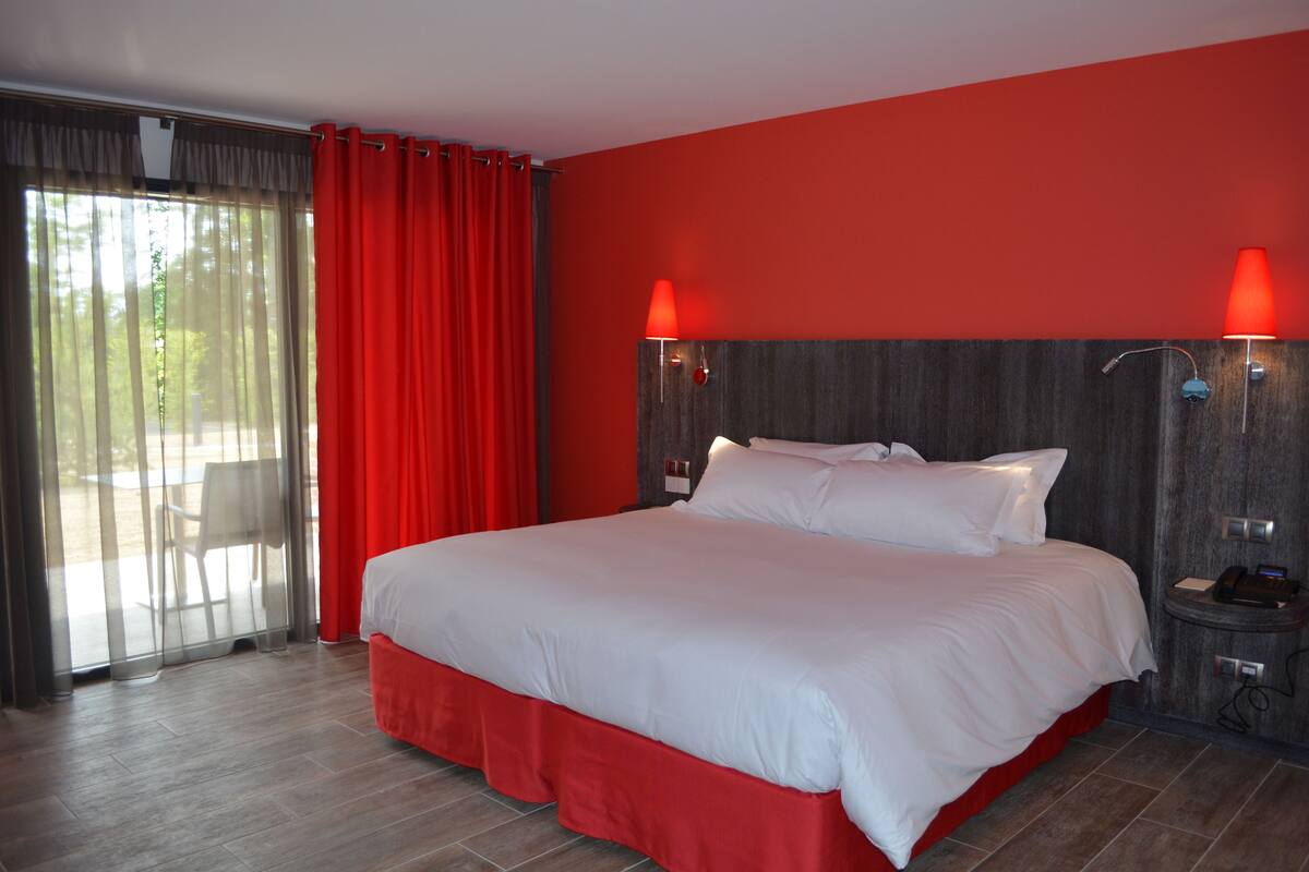 Une chambre d’hôtel avec un grand lit, des rideaux rouges et deux lampes fixées au mur.
