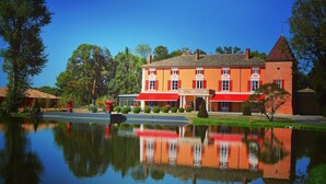 Een groot, tweelaags gebouw met een rood-witte gevel, dat weerspiegeld wordt in een rustig waterlichaam ervoor.
