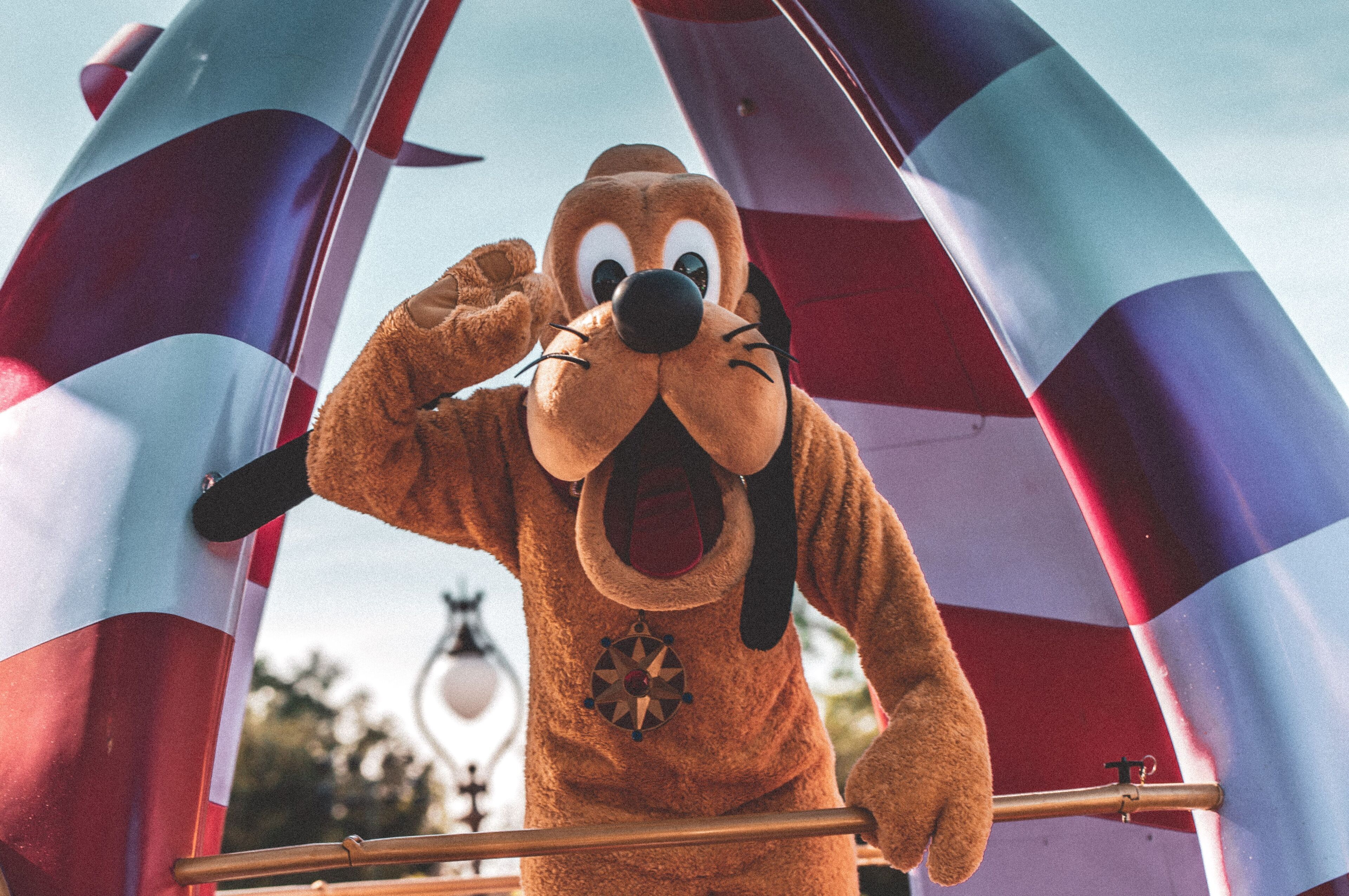 A person in a brown bear costume with a star emblem, standing in front of a striped archway.