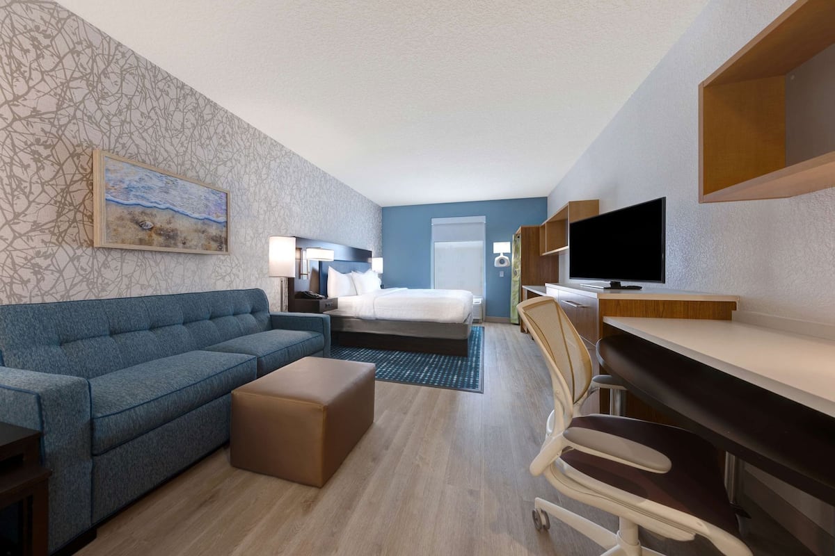 Hotellihuone, jossa on sänky, sininen sohva, kirjoituspöytä, jossa on televisio, ja tuoli.