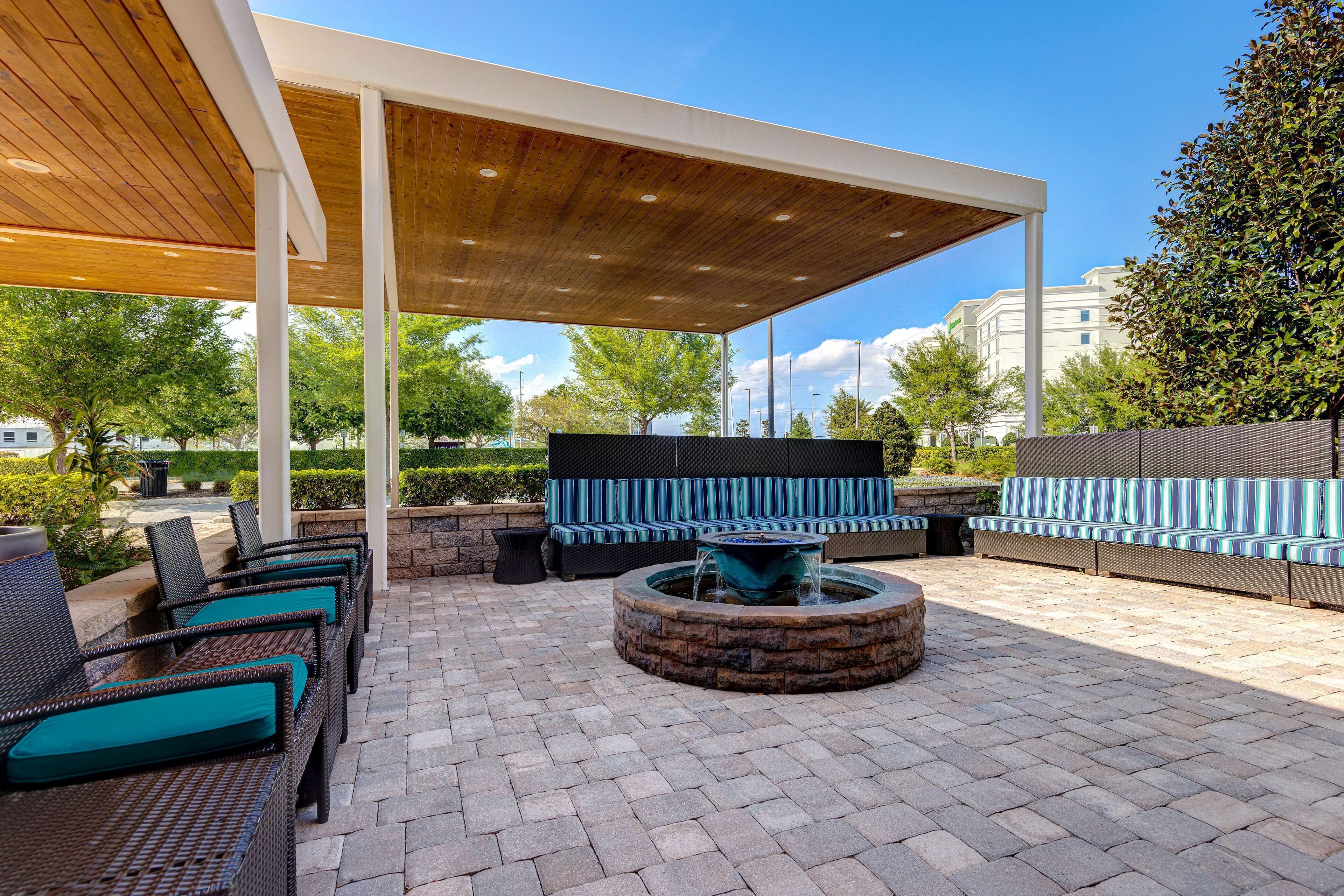 An outdoor patio with wicker furniture, a stone fire pit, and a covered seating area.