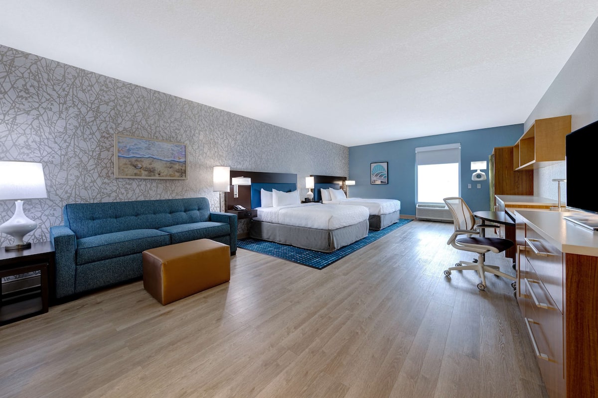 Hotellihuone, jossa on sininen sohva, sänky, työpöytä ja televisio.