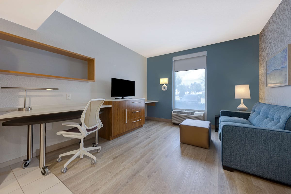 Moderni hotellihuone, jossa on työpöytä, tuoli, sohva ja suuri ikkuna.