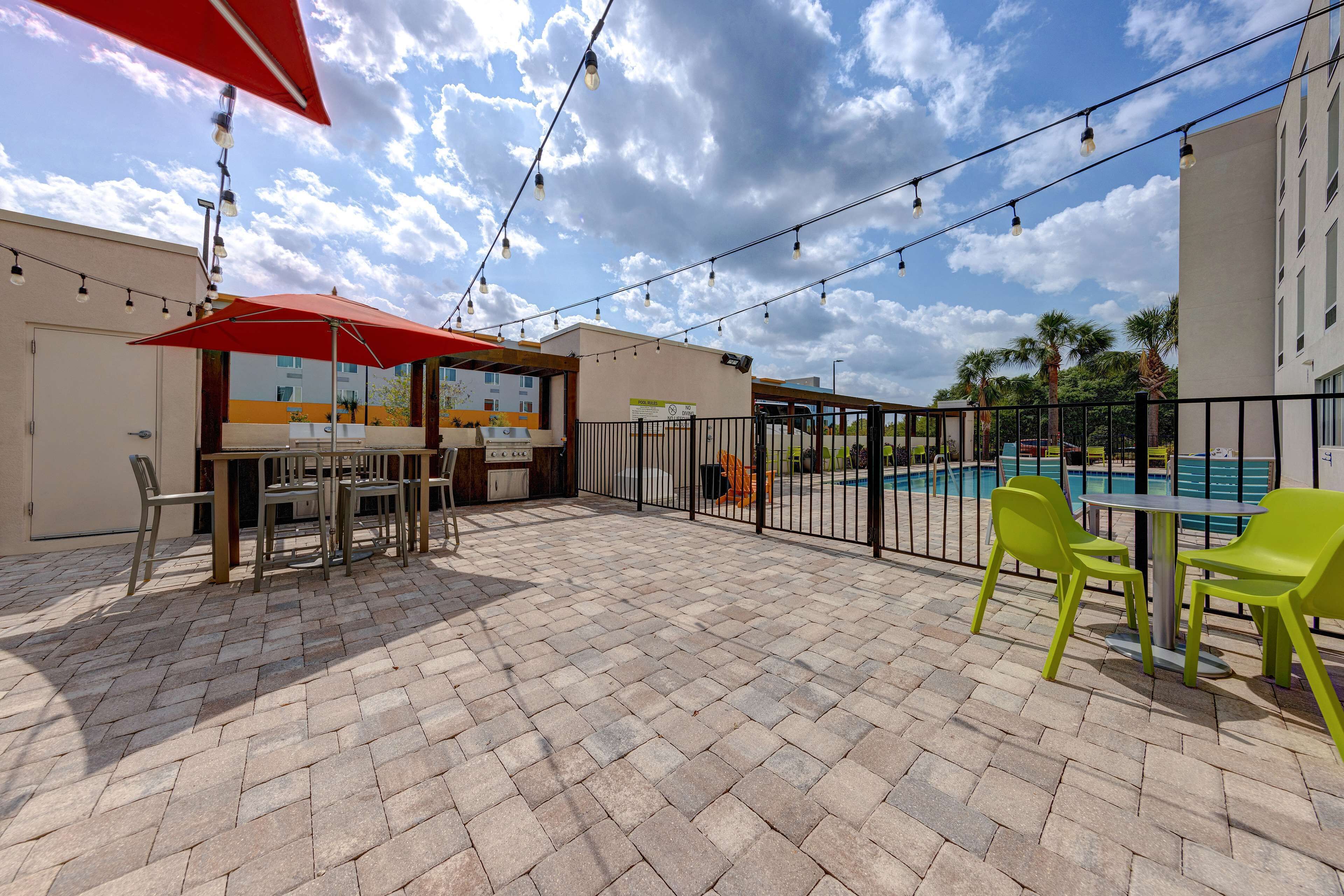 An outdoor patio with a pool, tables, chairs, and string lights.