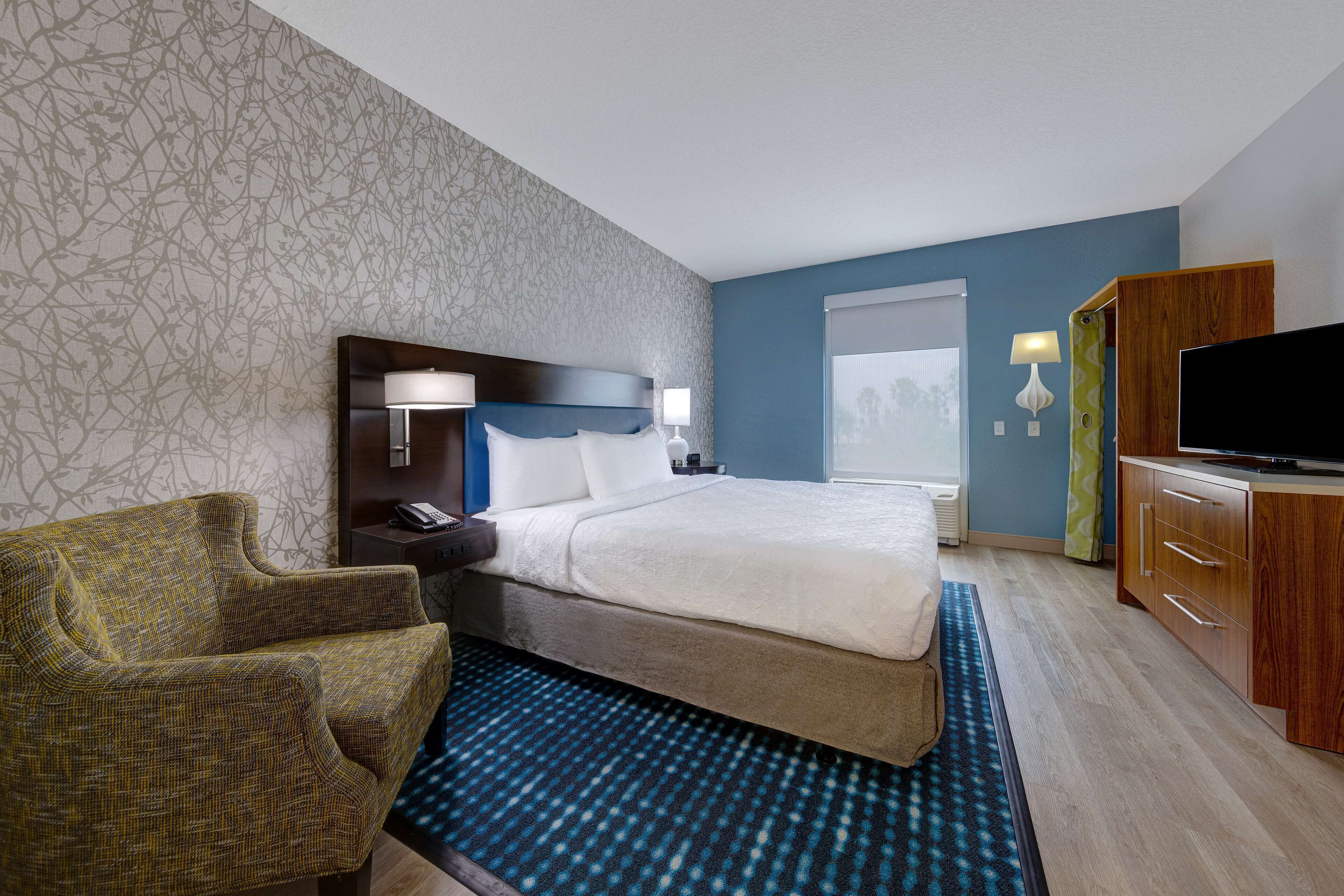 A hotel room with a bed, a desk, a chair, a TV, and a window.