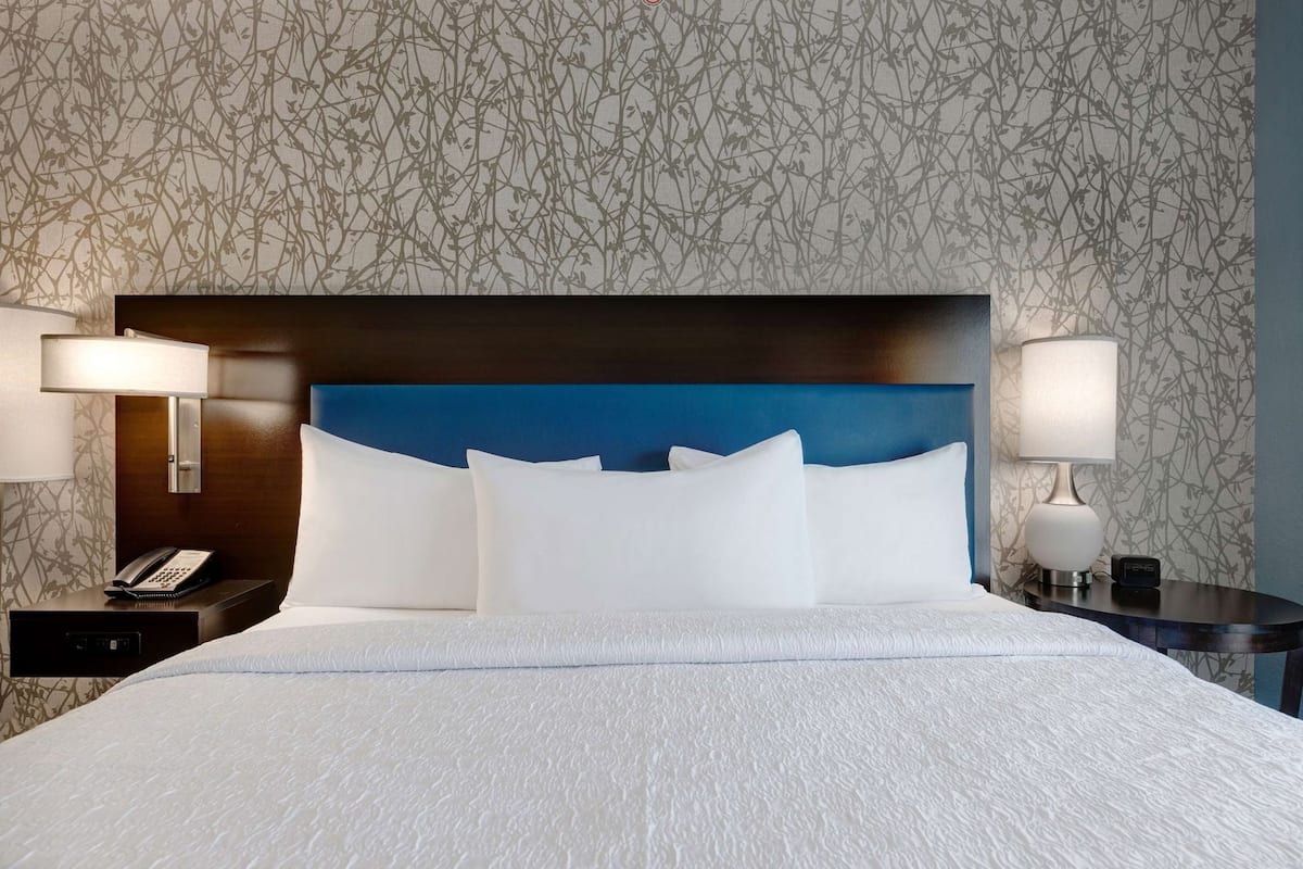 Hotellihuone, jossa on suuri sänky, sininen pääty, kaksi yöpöytää valaisimineen ja puhelin.