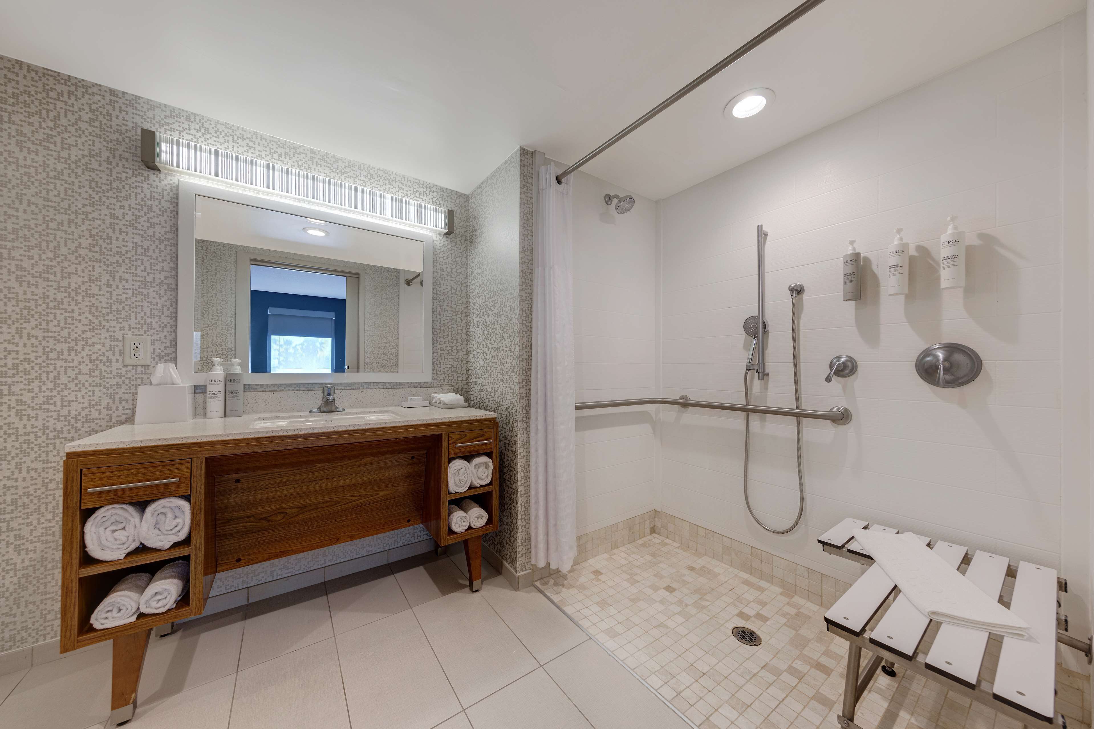 Un baño moderno con tocador de madera, ducha con barra de apoyo y piso de baldosas.