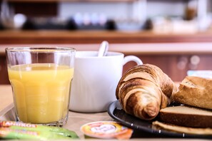 A breakfast tray with a glass of orange juice, a white mug, croissants, and slices of bread.