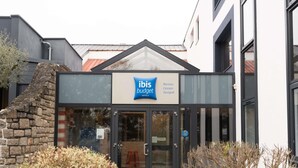 A hotel entrance with a glass door, a stone wall to the left, and a sign for ibis budget hotels. - ibis budget Rennes Cesson (Cesson-Sevigne)