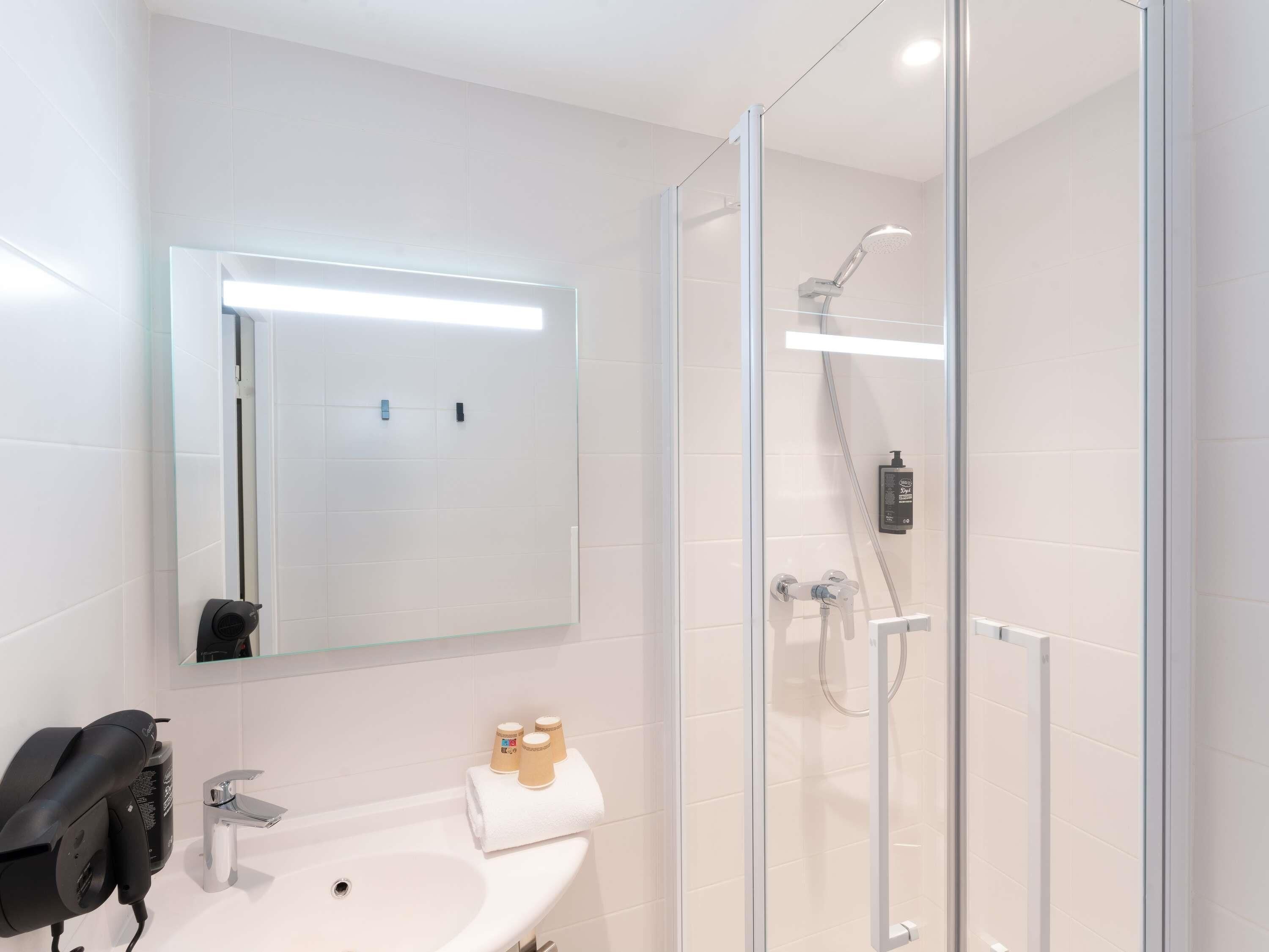 Une salle de bain moderne avec une douche à parois de verre, un lavabo blanc et un miroir au-dessus du lavabo.