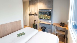 A modern hotel room with a bed, a desk, a TV mounted on the wall, and a window. - ibis budget Rennes Cesson (Cesson-Sevigne)