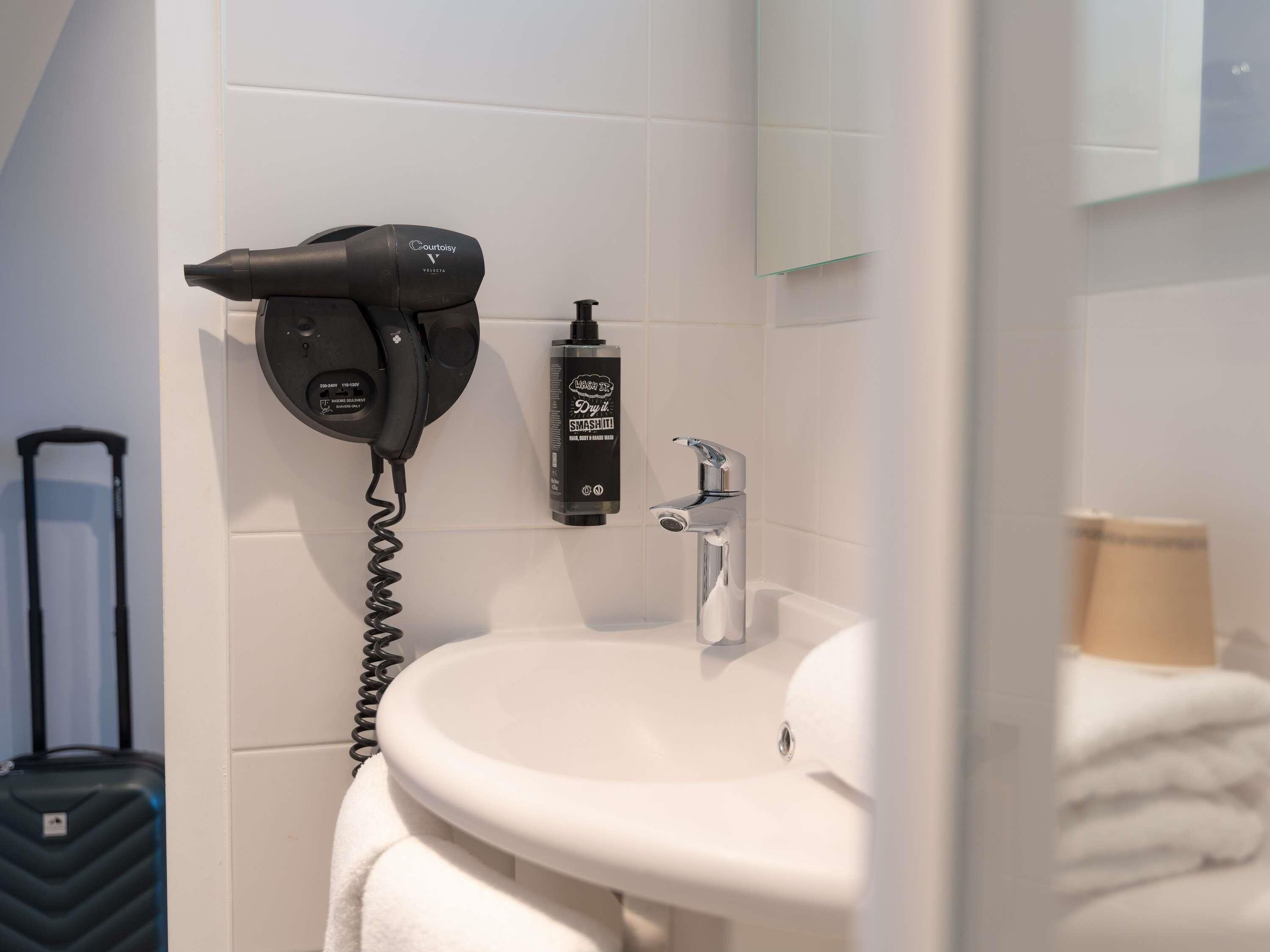 Un baño con secador de pelo, un frasco de producto capilar, un lavamanos y un espejo.