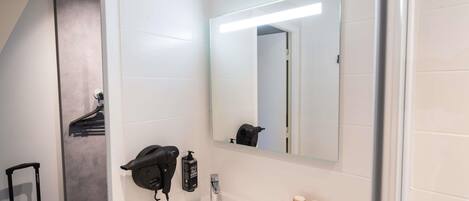 Un baño con lavamanos, espejo, secador de pelo y toallero.