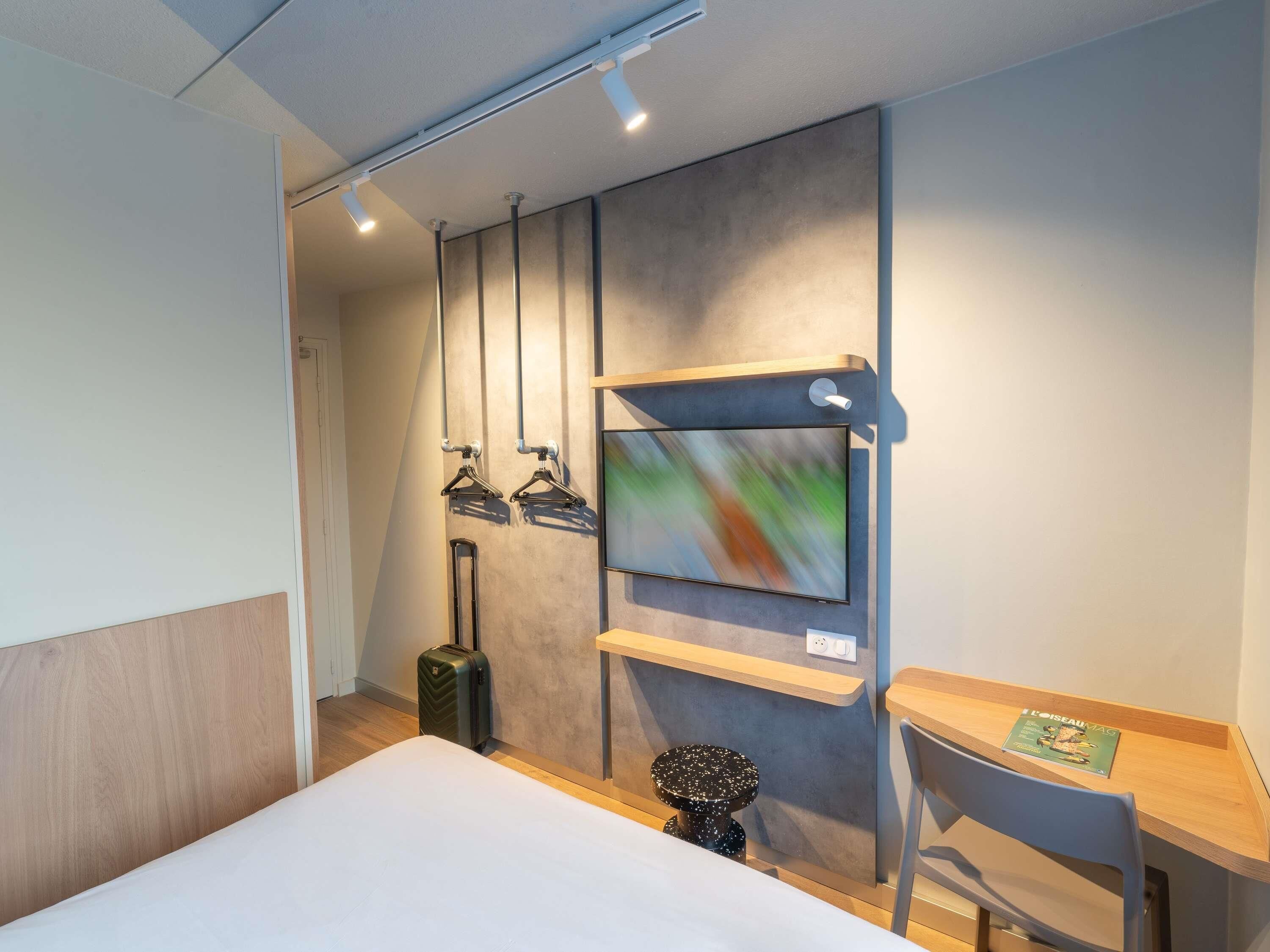 Habitación de hotel con cama, escritorio, silla, televisor en la pared y maleta en el suelo.