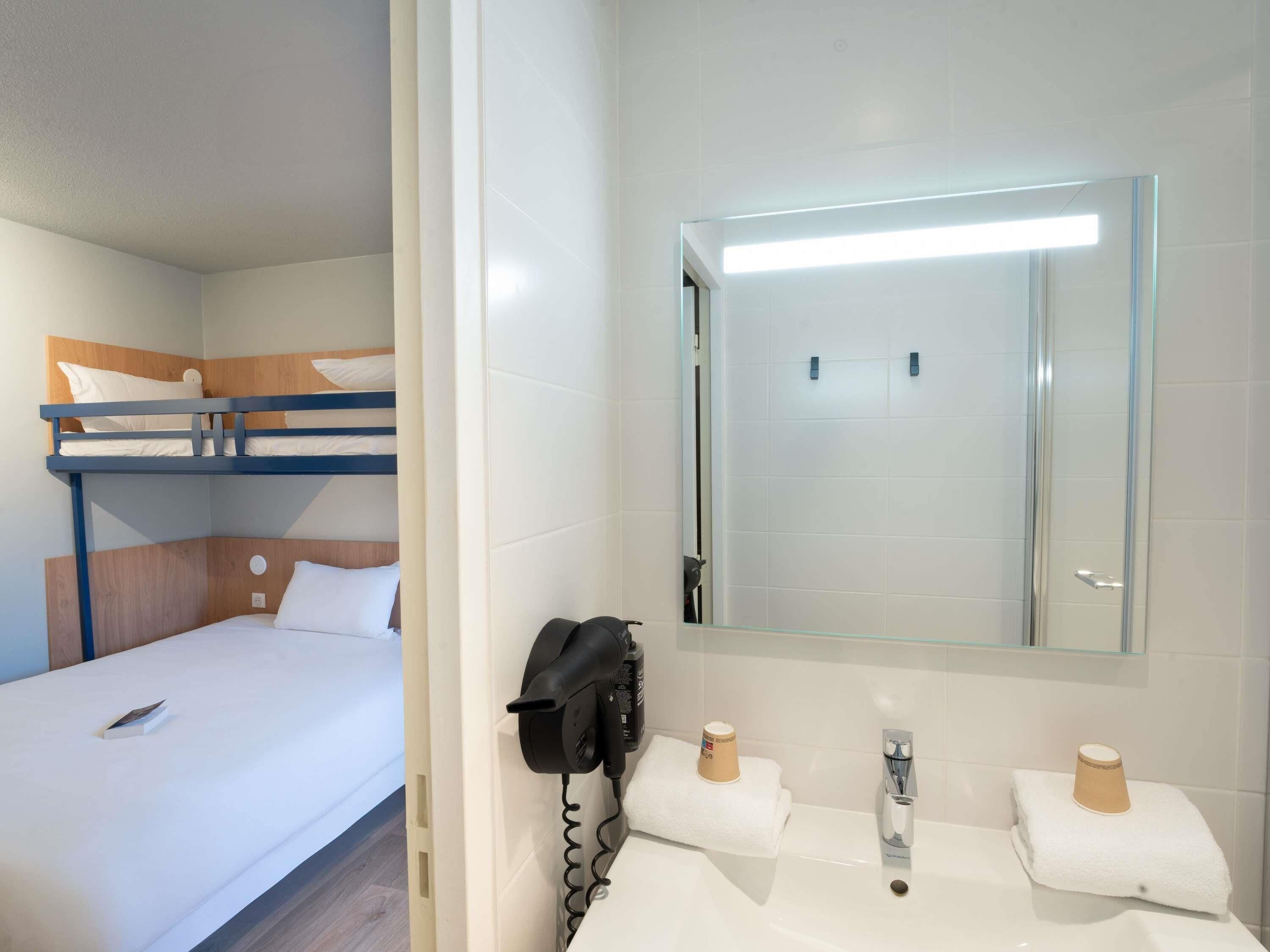 A hotel room with a bunk bed, a bathroom with a sink, mirror, and towel rack.