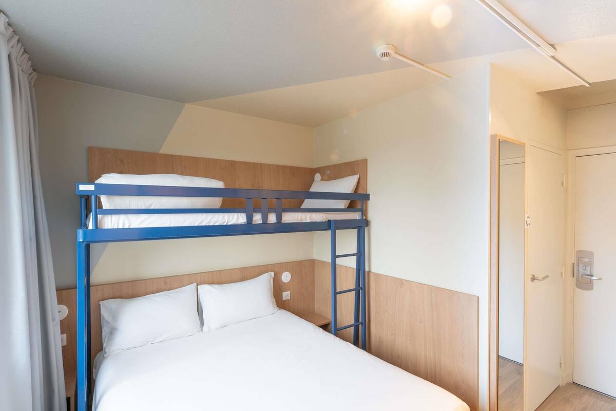 A bunk bed room with a wooden headboard, a white mattress, and a door in the background.