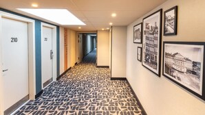 A hotel hallway with numbered doors, patterned carpet, and framed pictures on the walls. - ibis budget Rennes Cesson (Cesson-Sevigne)