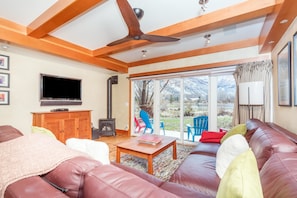 A living room with a leather sofa, a wooden coffee table, a television, and a large window with a view of the outdoors.
