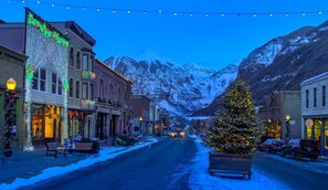 A snow-covered street with buildings and a Christmas tree in the center.