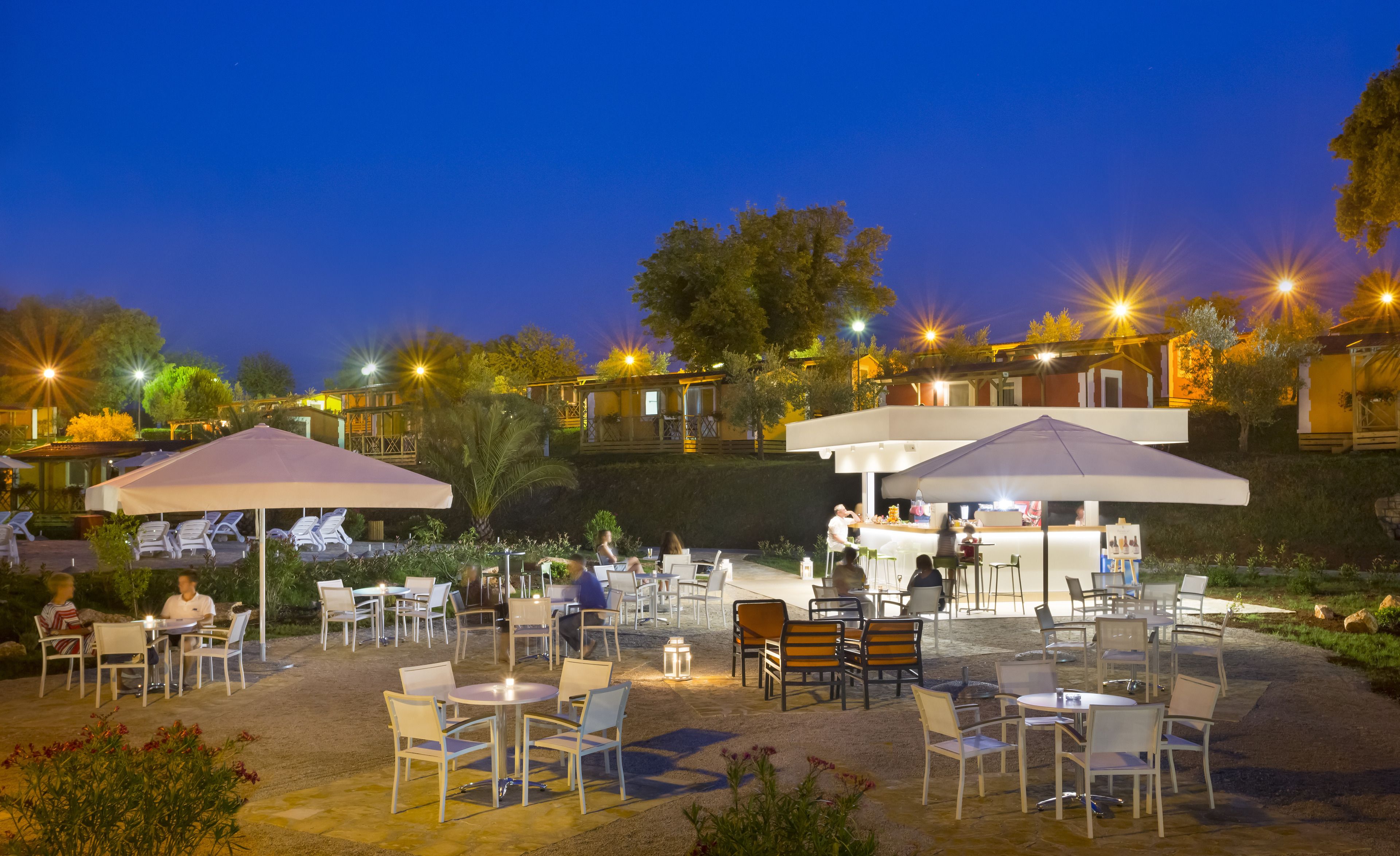 An outdoor dining area with tables and chairs, umbrellas, and a bar area with a counter.