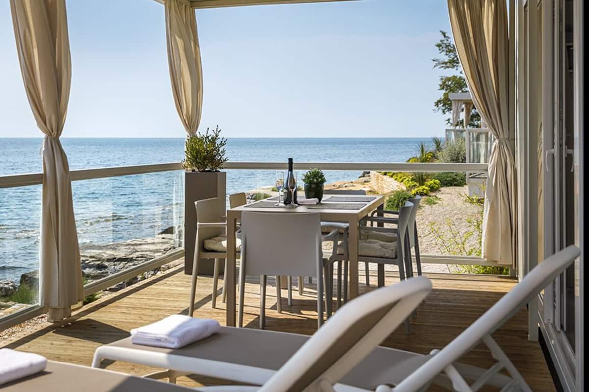 Une terrasse avec vue sur la mer, comprenant une table et des chaises, une plante en pot et une bouteille.