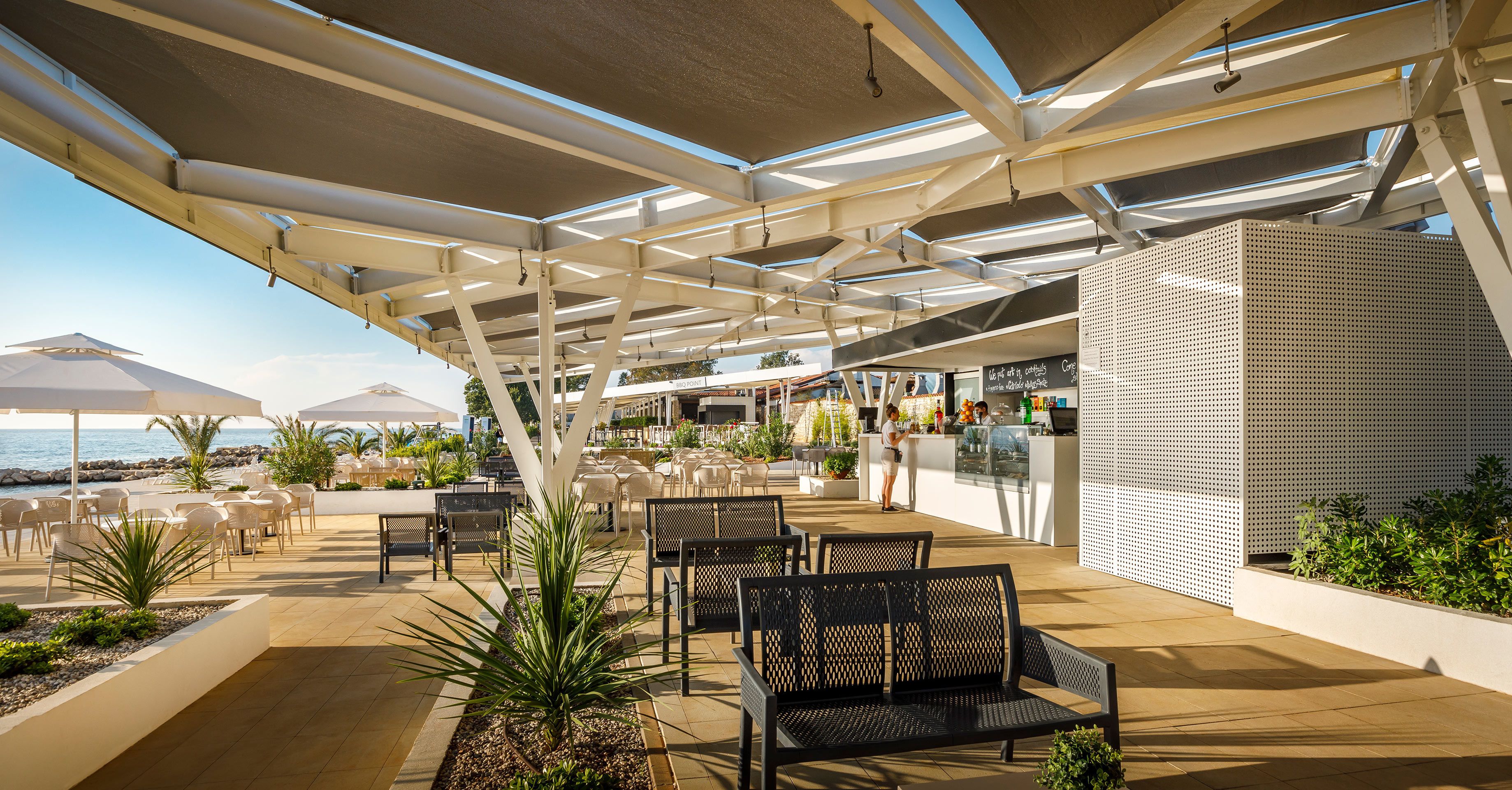 Un espacio al aire libre con mesas, sillas, una barra y vistas al mar.