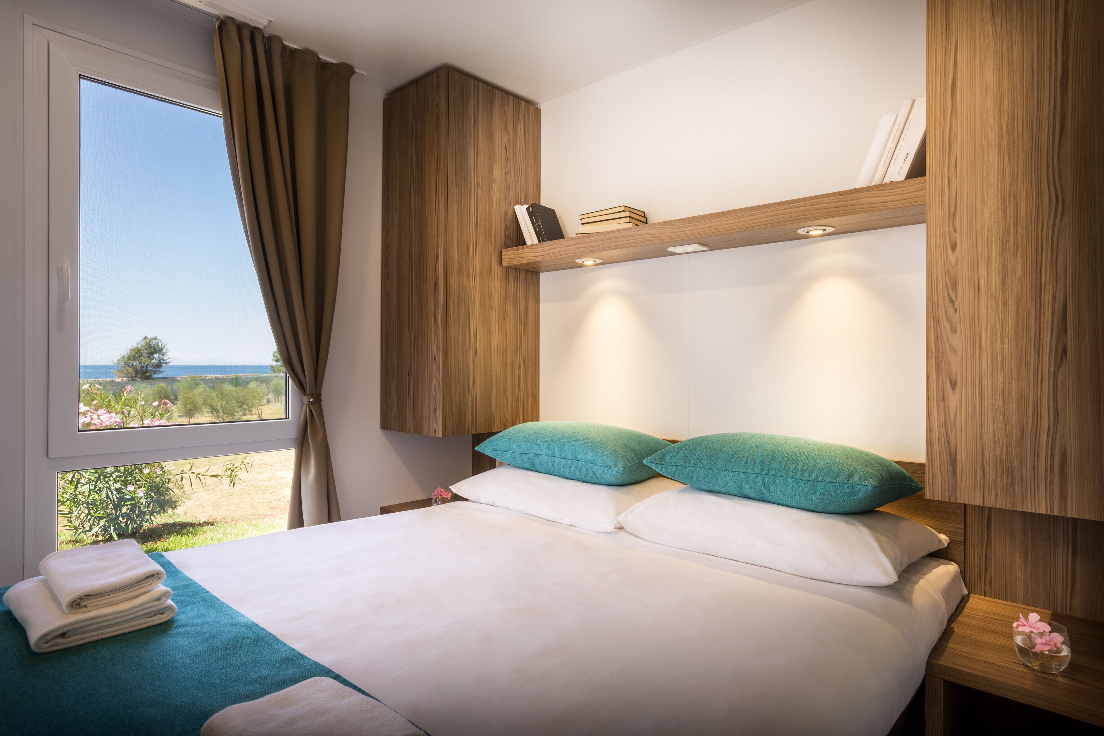 A bedroom with a large bed, a view of the outdoors, and wooden paneling.