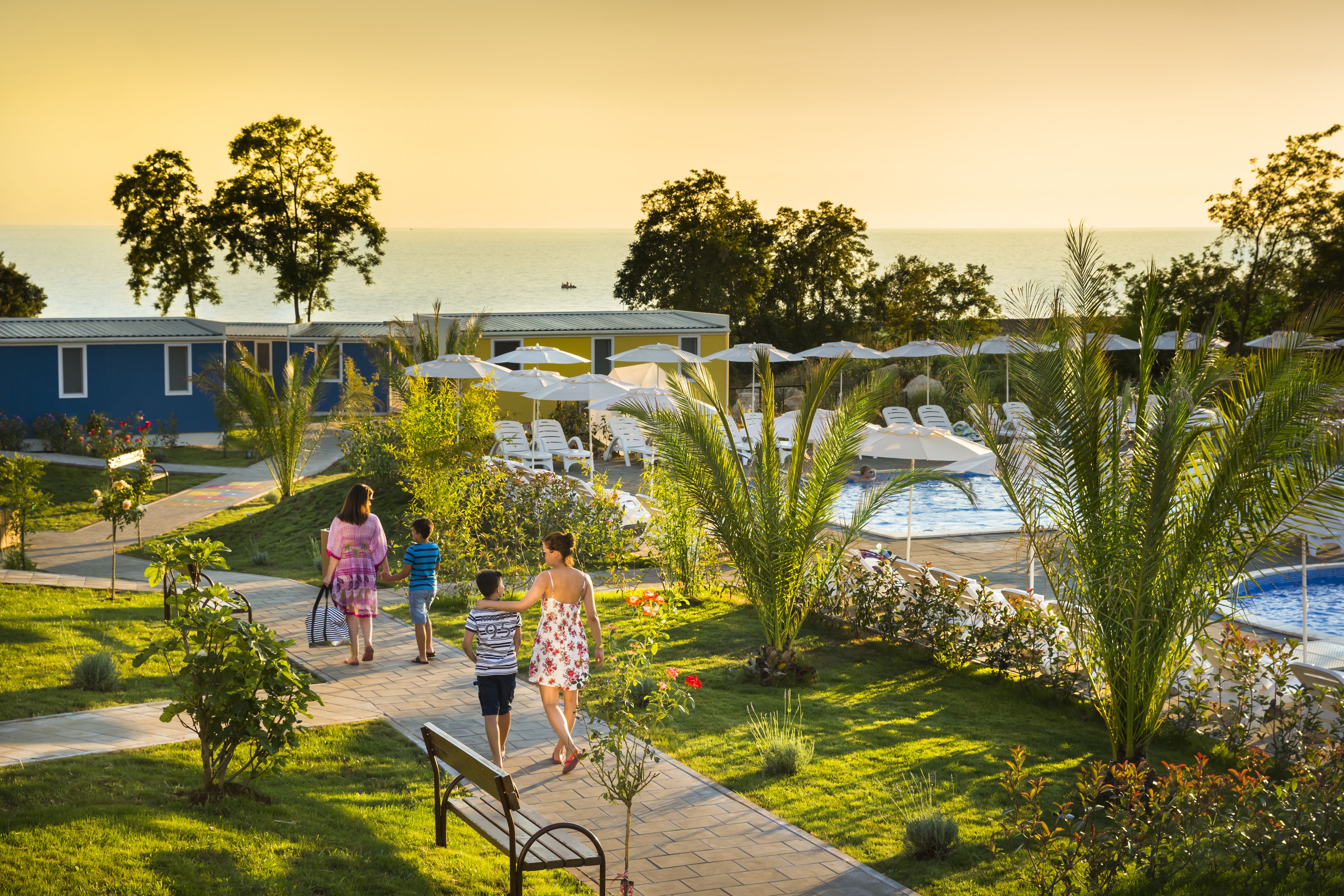 A pathway leading to a pool area with lounge chairs and umbrellas, surrounded by greenery and overlooking a body of water.