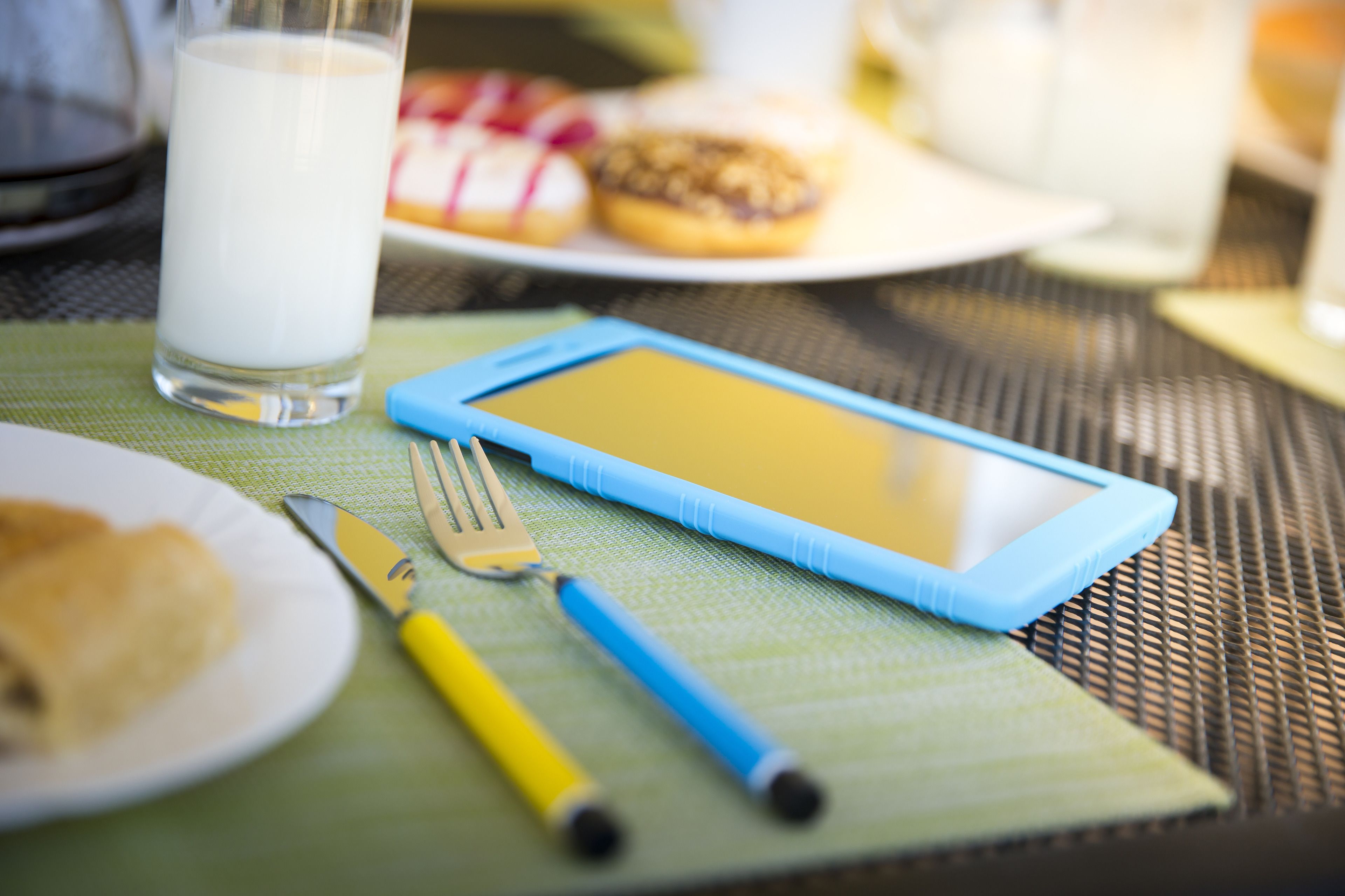 Un tablet su un tavolo con una forchetta, un coltello e un bicchiere di latte.