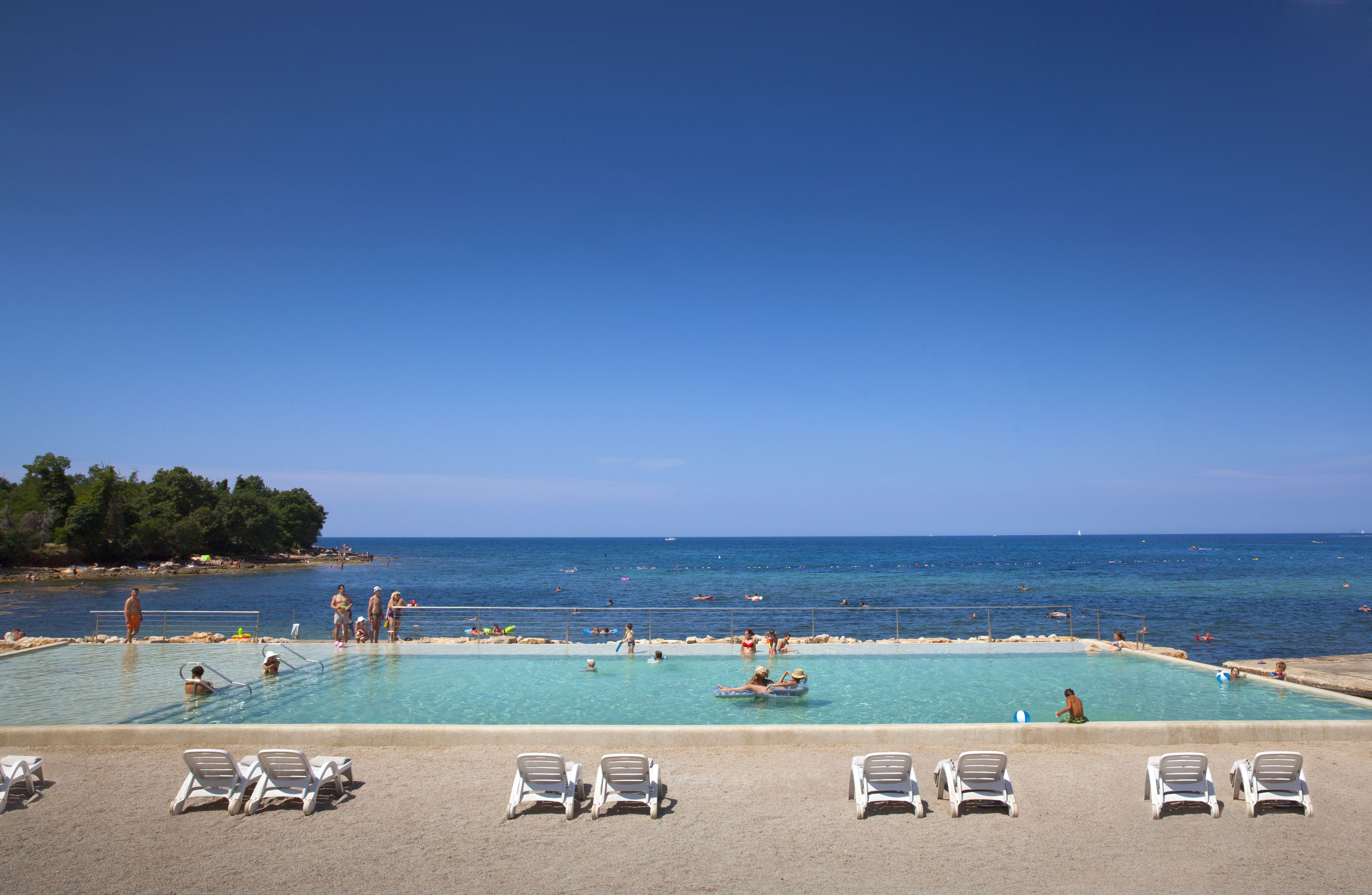 Zona de piscina con sillones de descanso, piscina y vista al mar.