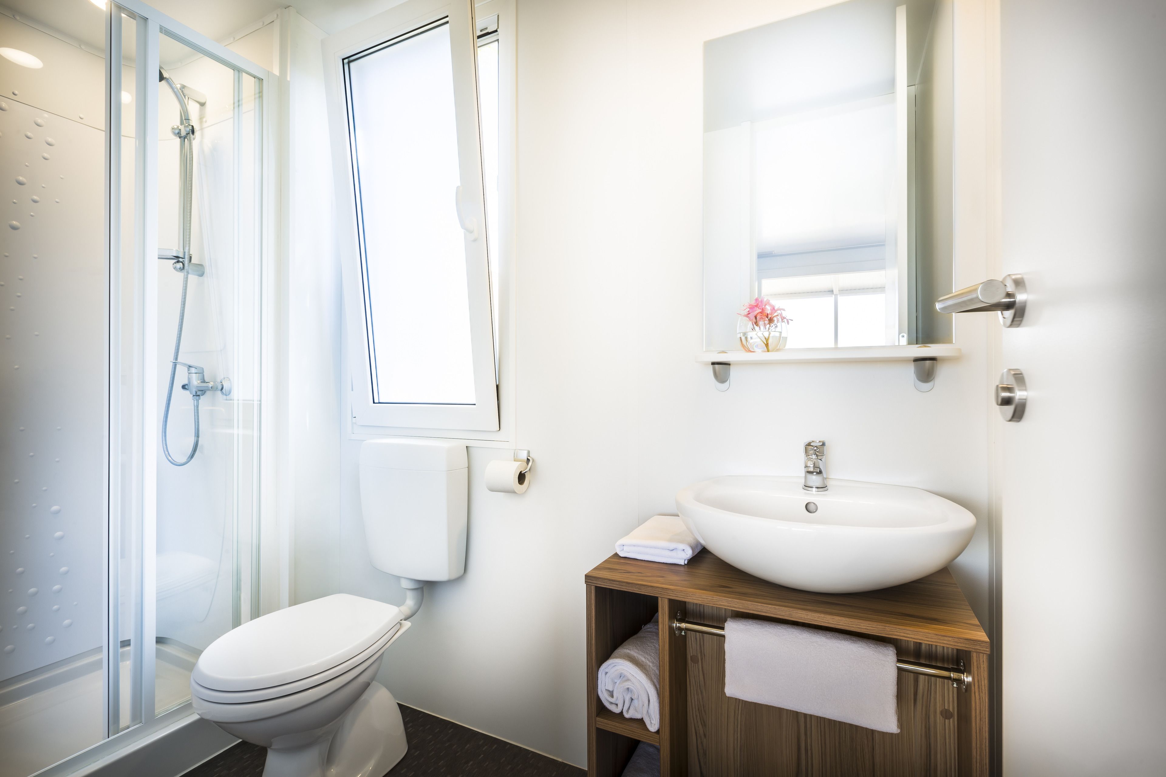 Une salle de bain moderne dotée d’une douche à parois de verre, de toilettes, d’un lavabo avec un meuble-vasque en bois et d’un miroir au-dessus du lavabo.