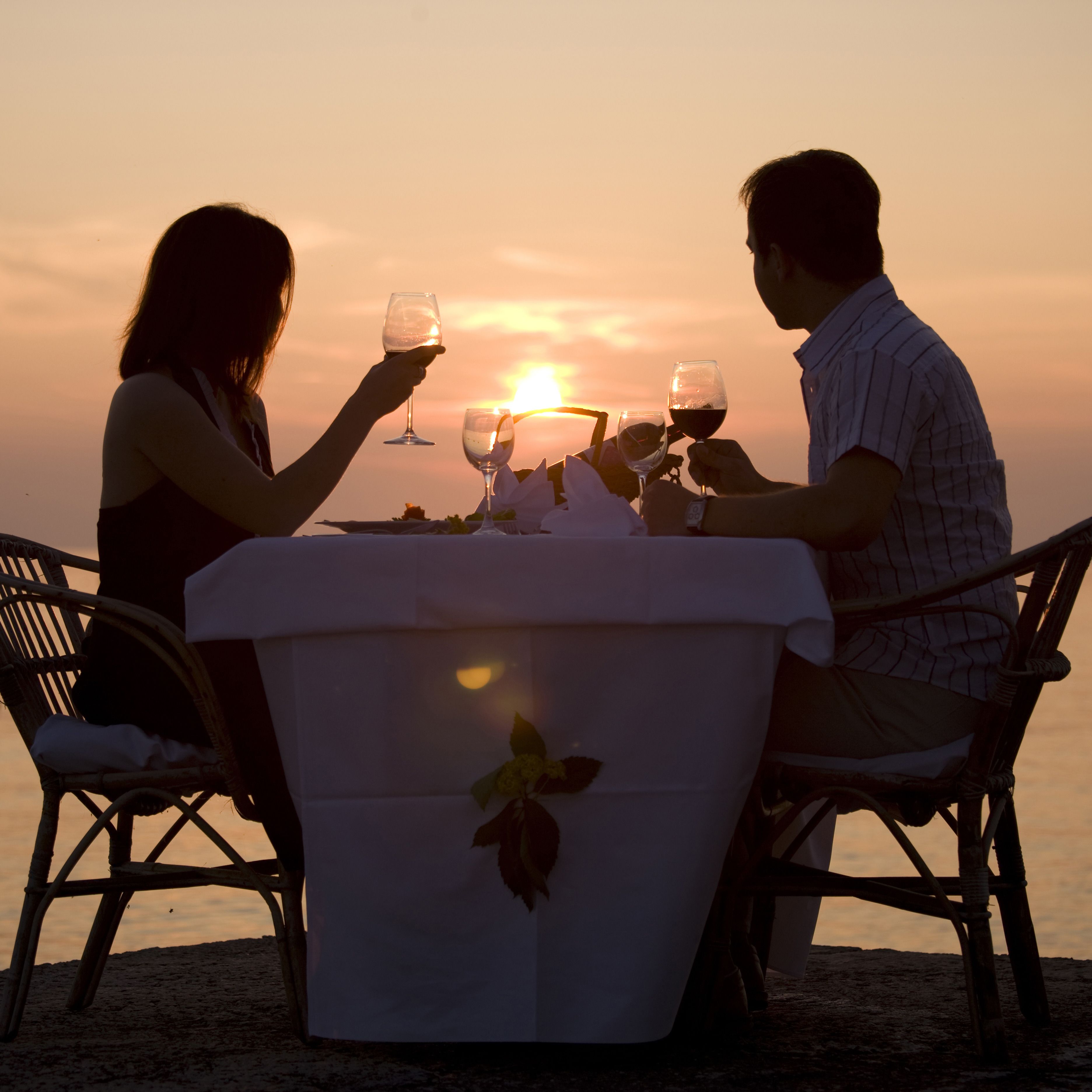 Una pareja en una mesa, brindando copas de vino con vistas al atardecer.