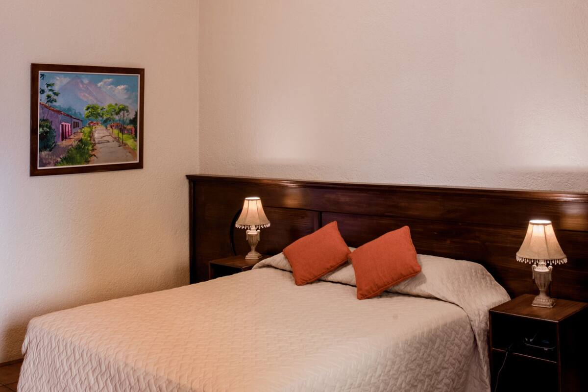 A bedroom with a bed, two bedside lamps, a ceiling fan, and a framed picture on the wall.