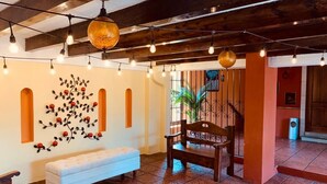 A lobby with a white bench, a wooden bench, and a wall art piece. - Hotel Villa Española (Guatemala City)