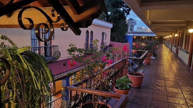 A covered outdoor area with potted plants and a railing. - Hotel Villa Española (Guatemala City)