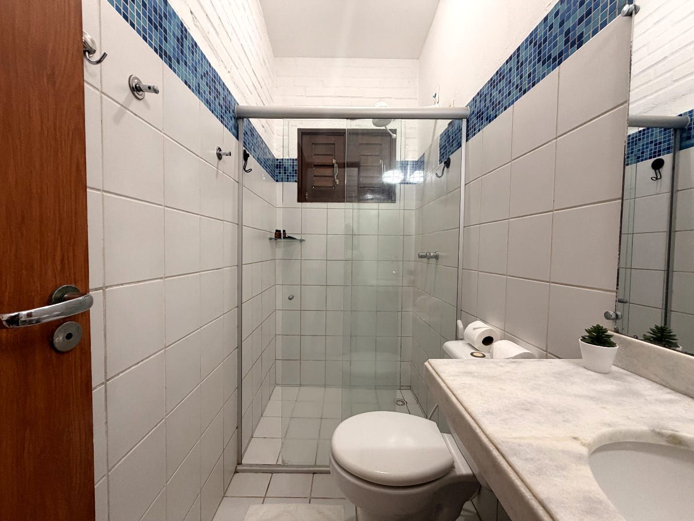A bathroom with a glass-enclosed shower, a toilet, and a sink with a mirror.
