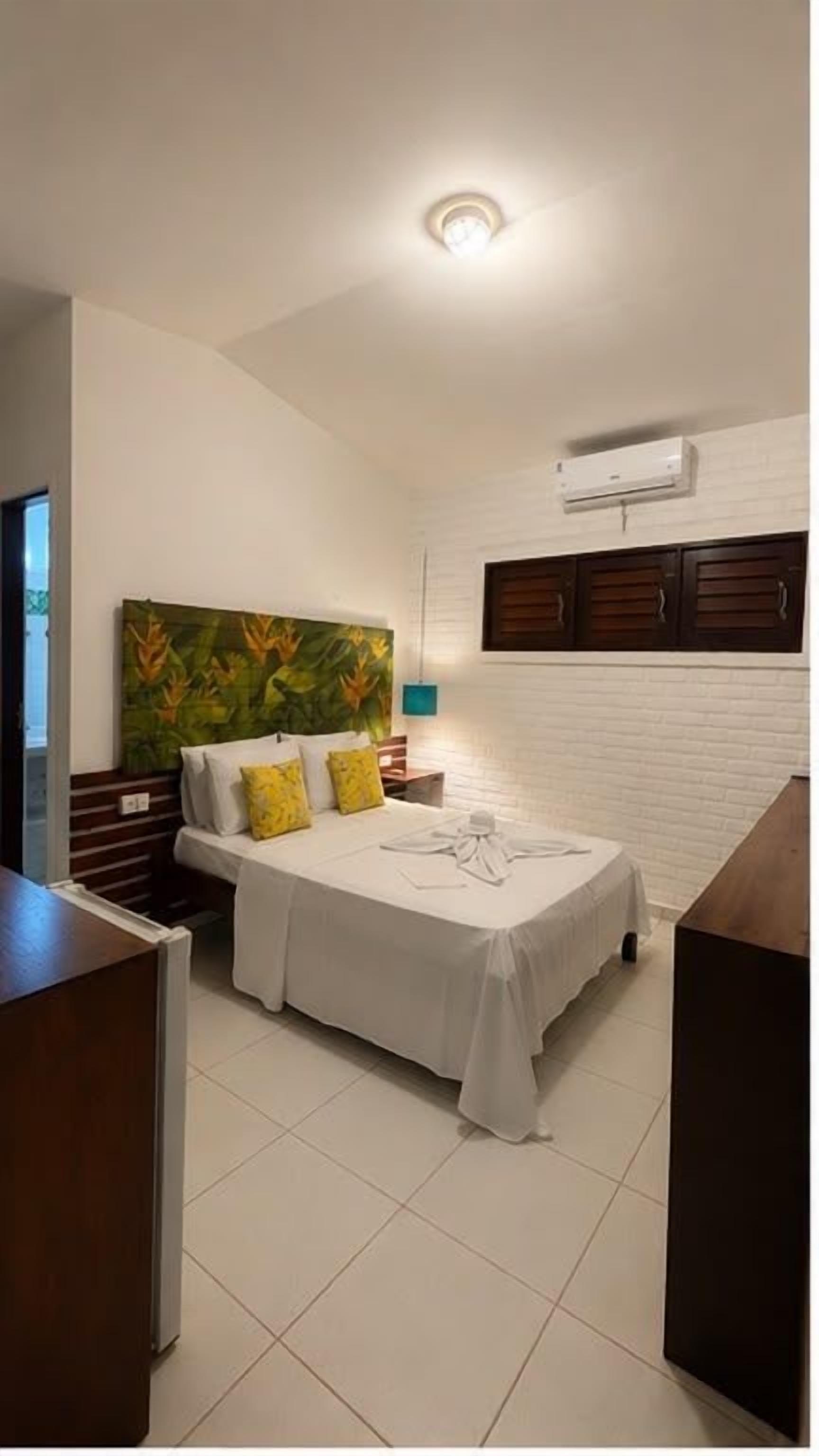 A bedroom with a bed, a nightstand, a wall-mounted air conditioner, and a window with curtains.