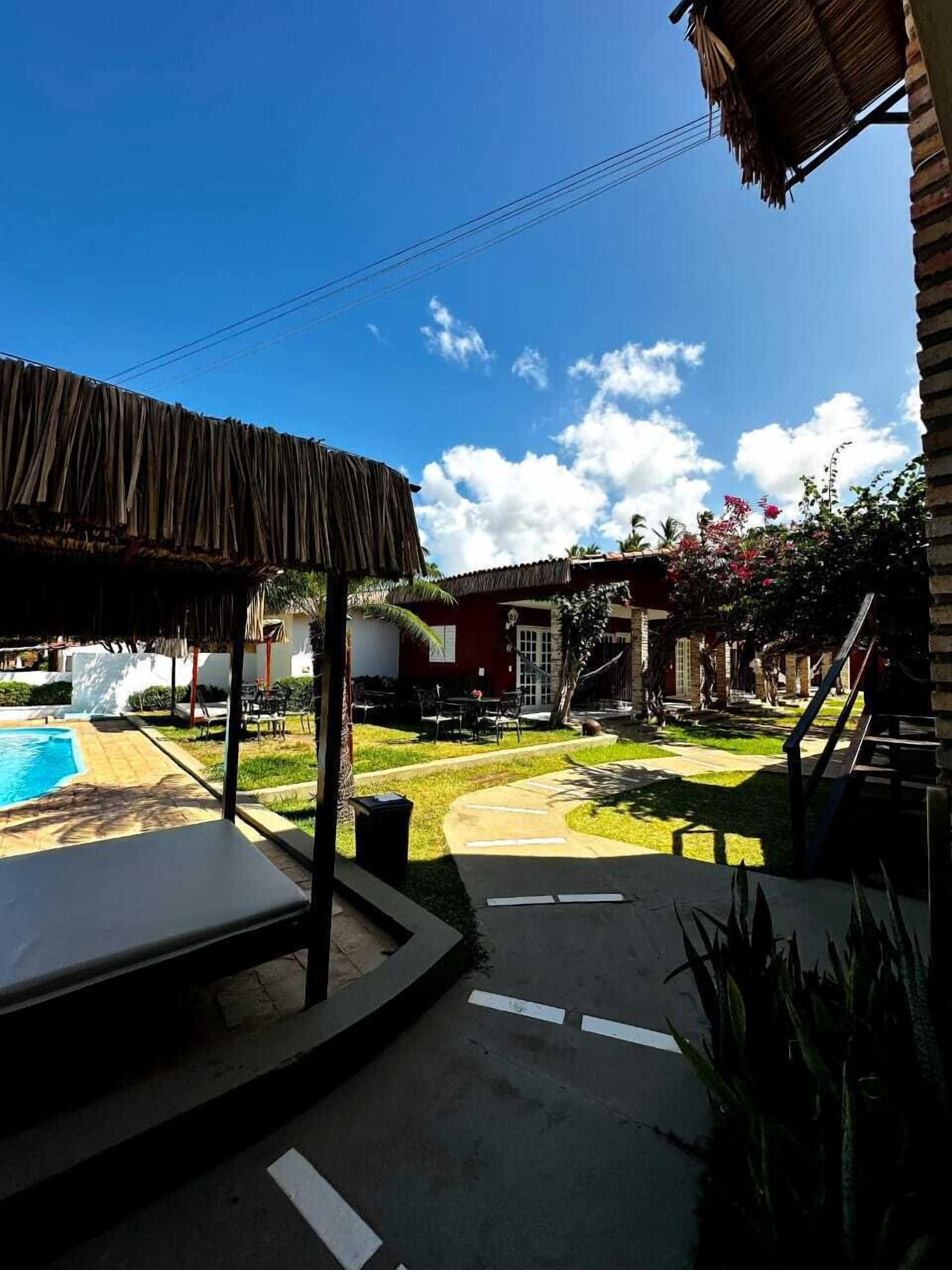 A pool area with a thatched roof structure, a clear blue sky, and a well-maintained lawn.